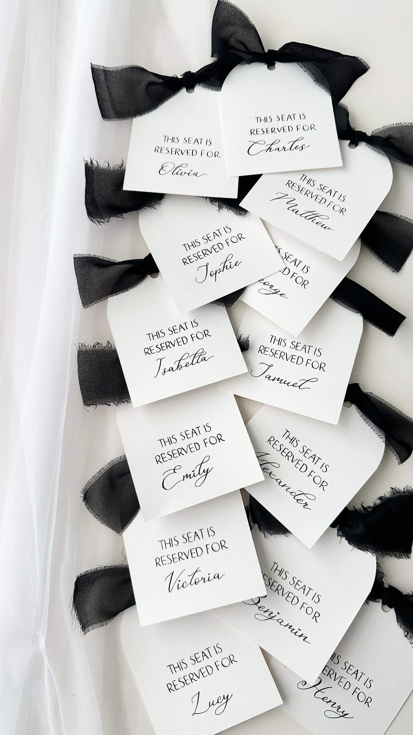 White 10x5 arch cards with handwritten calligraphy names in black ink finished with black ribbons on a white background