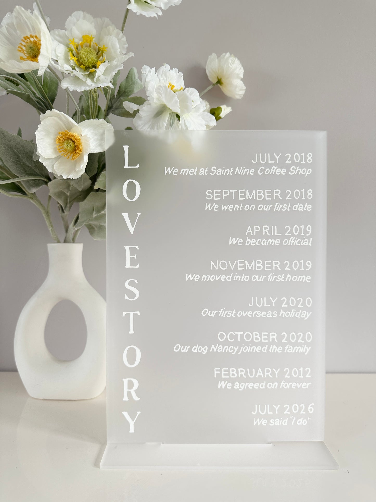 Frosted clear acrylic with white writing showing your love story. The words love story are written on the left hand side with on the right, the places and dates of the timeline of your love story such as ‘February 2012 we agreed on forever’ and ‘July 2026 we said I do’