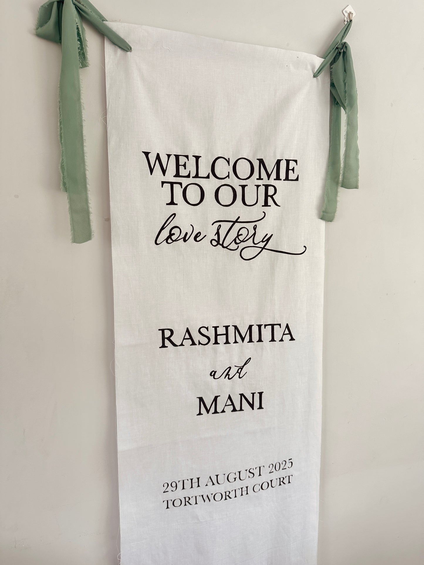 Personalized wedding towel with 'Welcome to our love story' text and names, hanging against a light background.