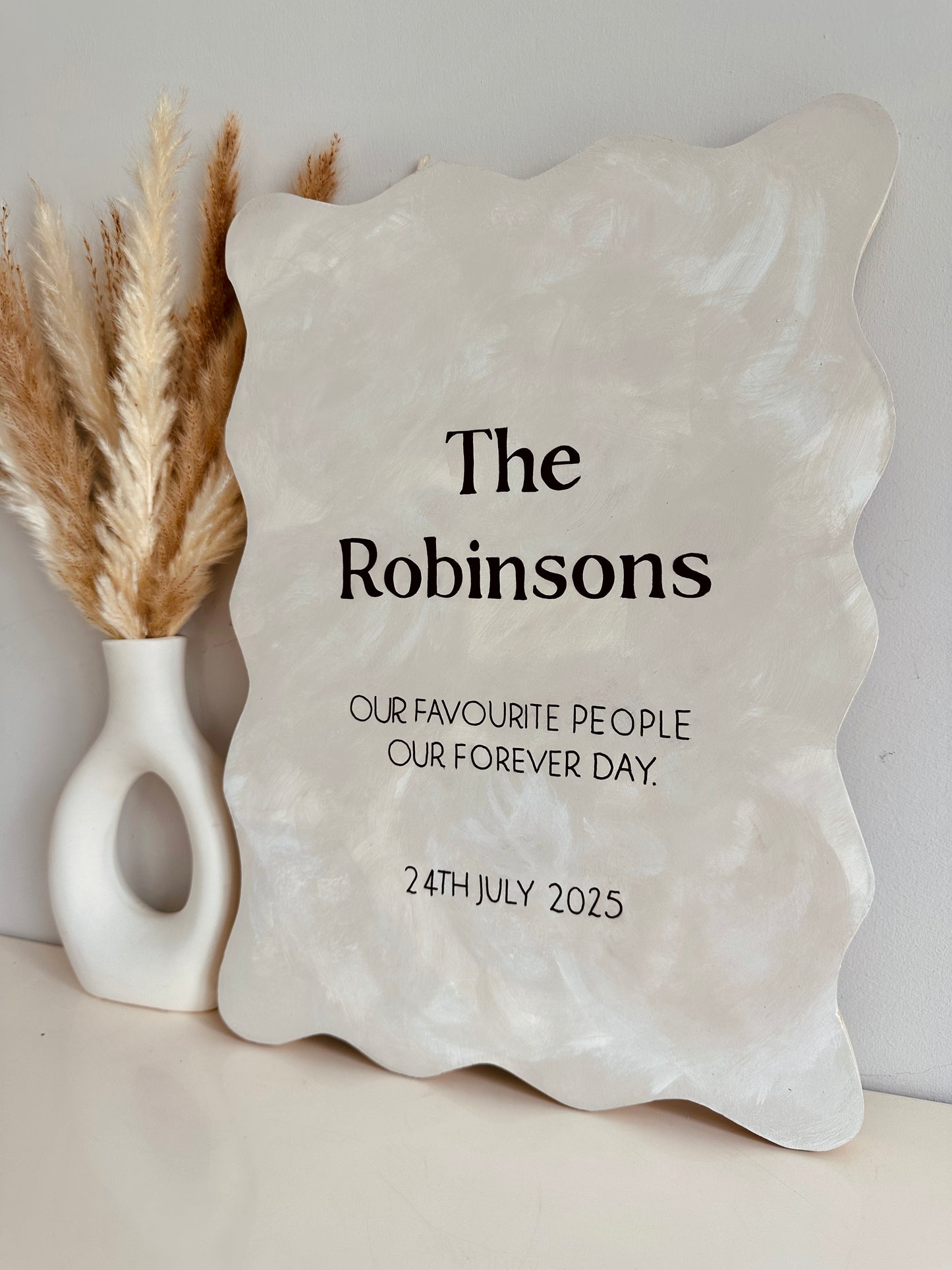 Custom wavy-edge wood sign for wedding decor in neutral tones. Decorative stone plaque with 'The Robinsons' text and personalised message on a neutral background.