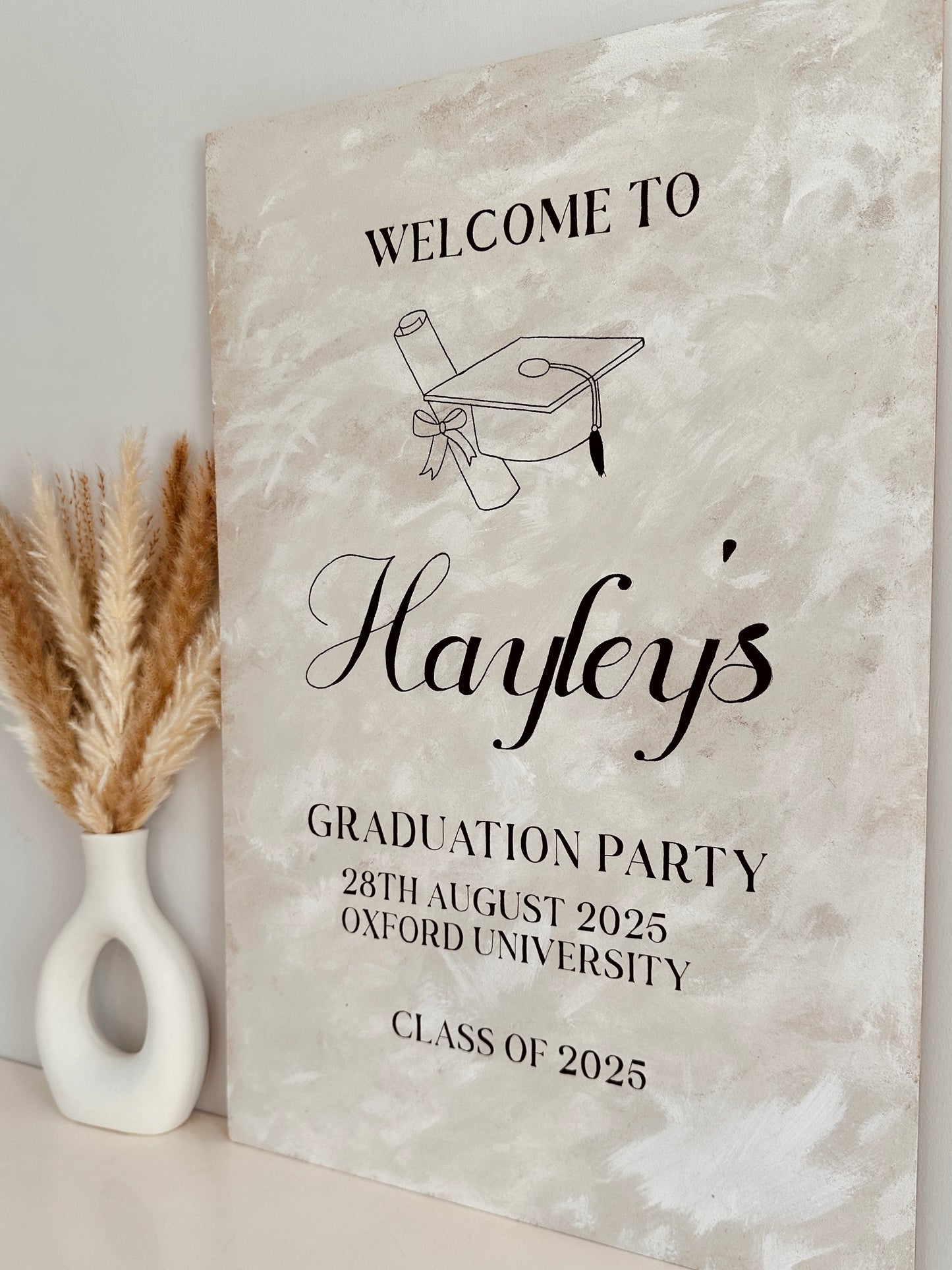 a1 wooden sign finished with a lime wash effect paint for a graduation ceremony. The sign includes the name of the person being celebrated along with the party type, date and location.