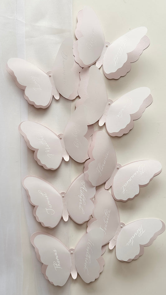 Blush pink shaped butterfly cardstock with layer vellum butterfly card to create a 3D effect, with first name on one side and last name on the other side written in white ink 
