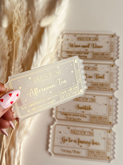 A close-up of a luxurious acrylic coupon reading "Afternoon Tea", held by a hand with heart-themed nail art, against a cozy aesthetic background.