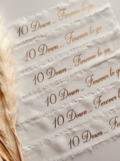 Custom white chiffon wedding ribbons featuring elegant gold calligraphy with couple’s names and wedding date, paired with pampas grass for boho wedding decor.