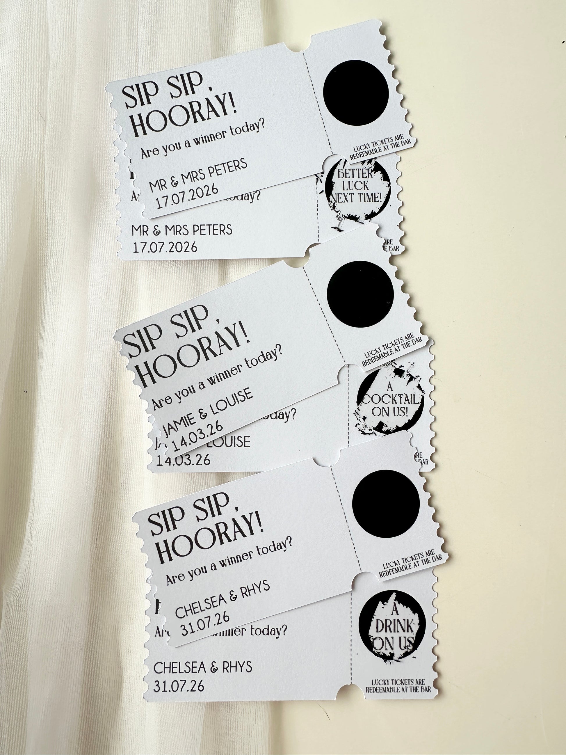 Set of three personalised tickets with black scratch ticket scratched off to reveal winning or loosing tickets next to an example ticket of sticker not yet scratched with names and dates on a white background