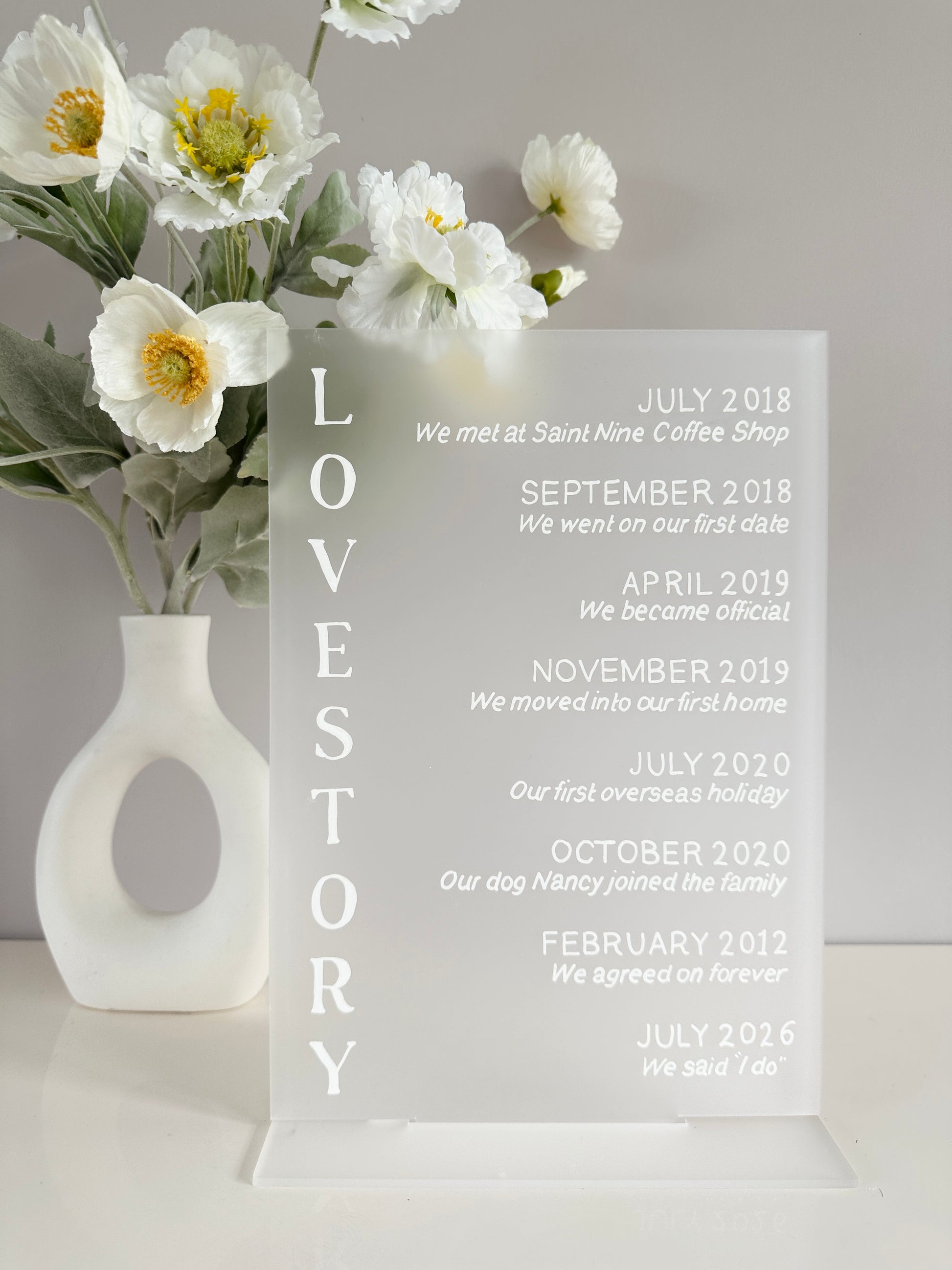 Frosted clear acrylic with white writing showing your love story. The words love story are written on the left hand side with on the right, the places and dates of the timeline of your love story such as ‘February 2012 we agreed on forever’ and ‘July 2026 we said I do’