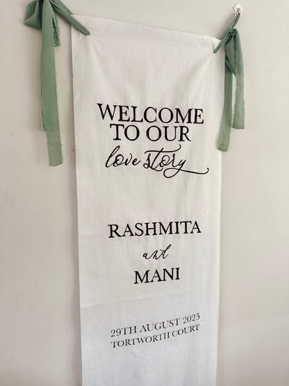 Personalized wedding towel with 'Welcome to our love story' text and names, hanging against a light background.