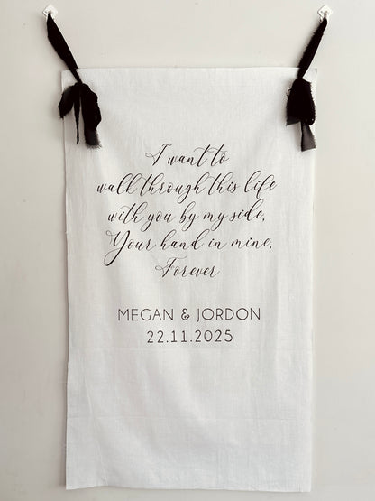 Personalized fabric with romantic quote and names, hanging on a white wall.