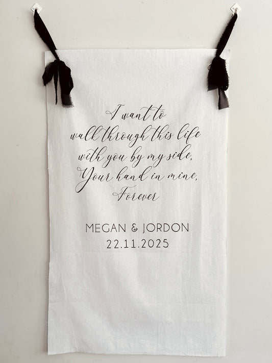 Personalized fabric with romantic quote and names, hanging on a white wall.