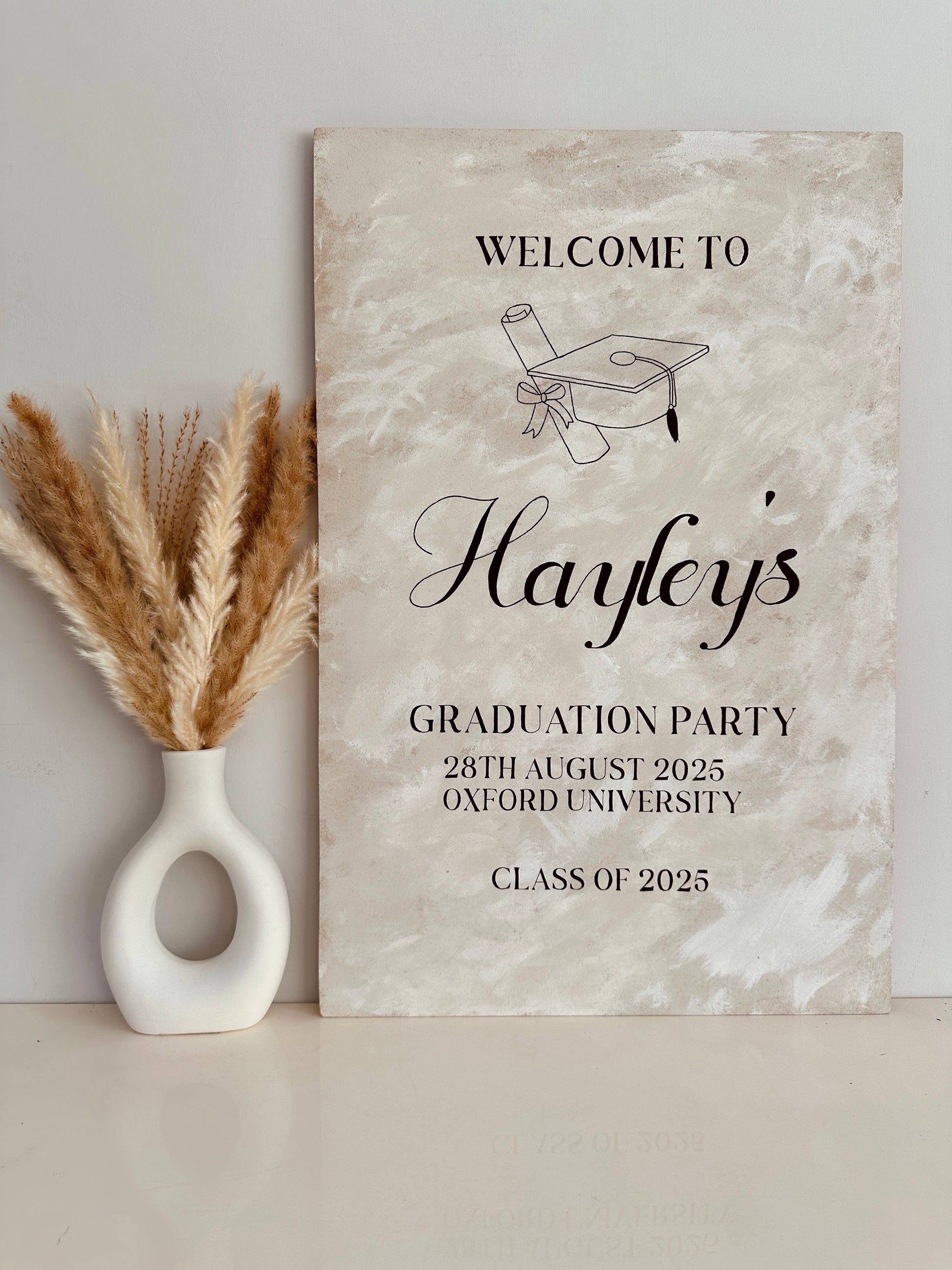 a1 wooden sign finished with a lime wash effect paint for a graduation ceremony. The sign includes the name of the person being celebrated along with the party type, date and location.