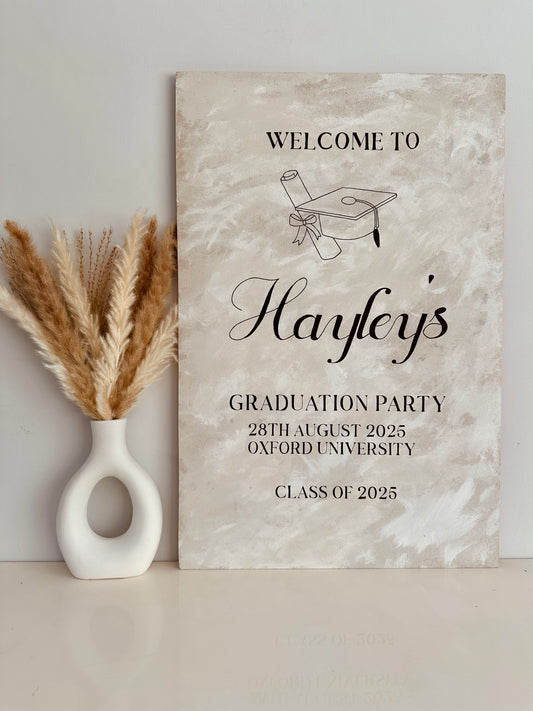 a1 wooden sign finished with a lime wash effect paint for a graduation ceremony. The sign includes the name of the person being celebrated along with the party type, date and location.