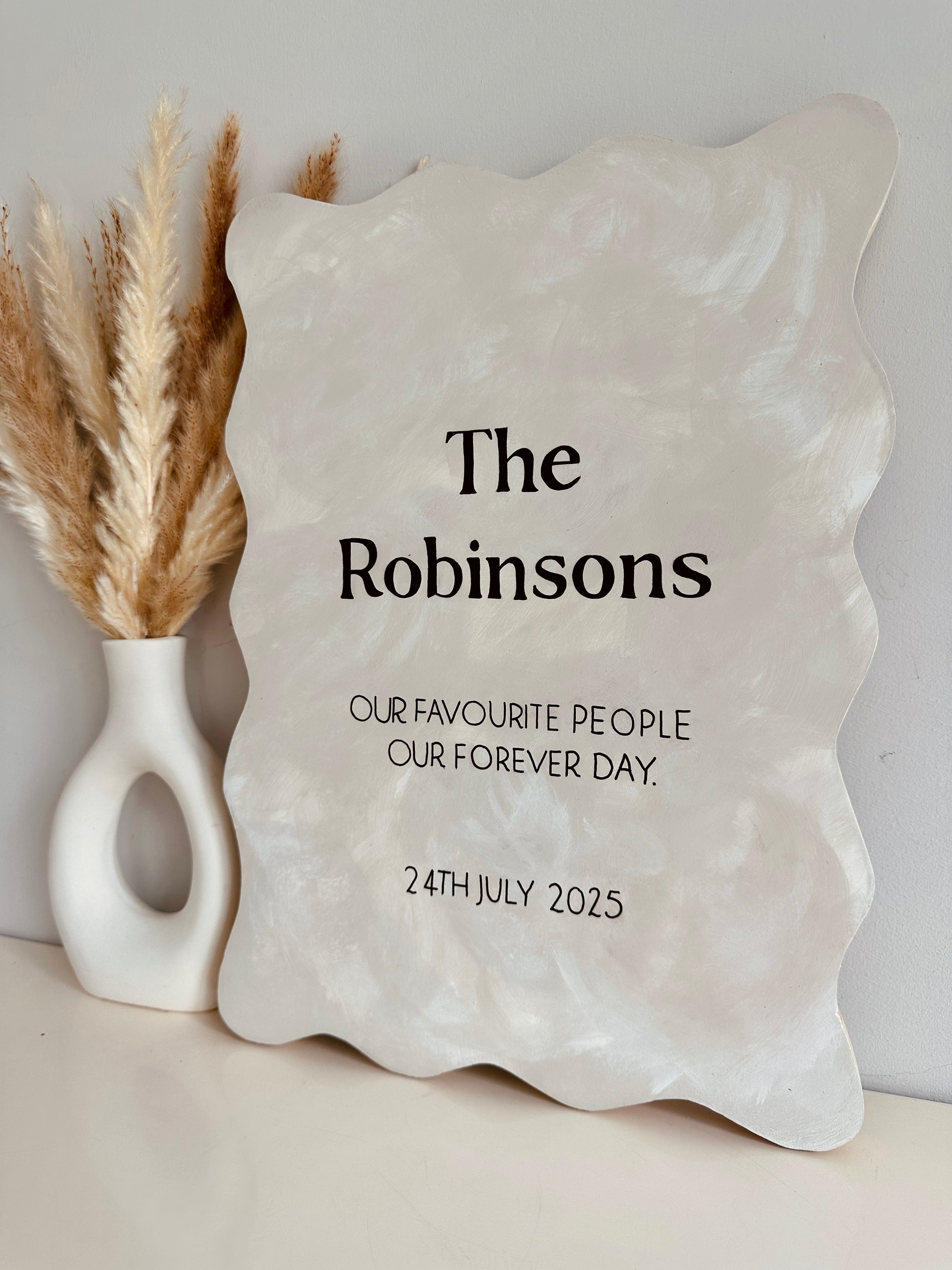 Custom wavy-edge wood sign for wedding decor in neutral tones. Decorative stone plaque with 'The Robinsons' text and personalised message on a neutral background.