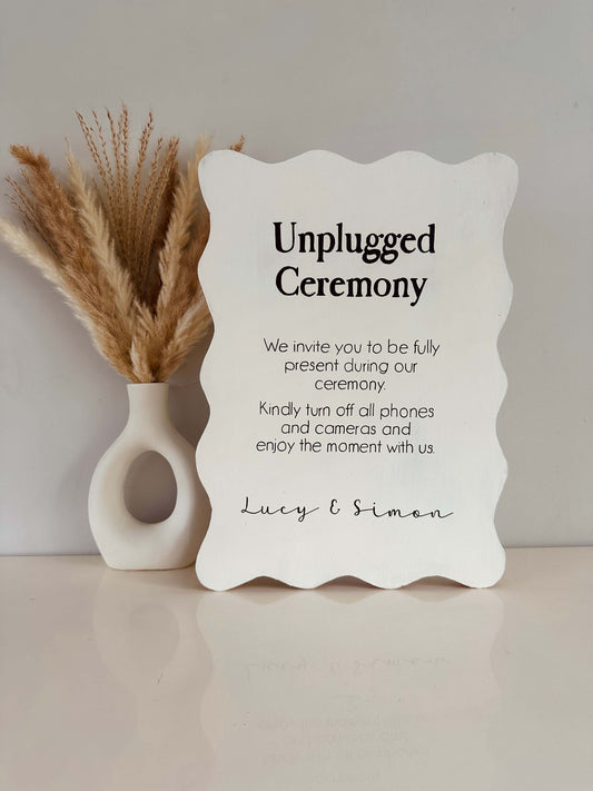 Unplugged ceremony sign with decorative vase on a neutral background. The freestanding 18mm thick sign is finished with black writing reading unplugged ceremony' 